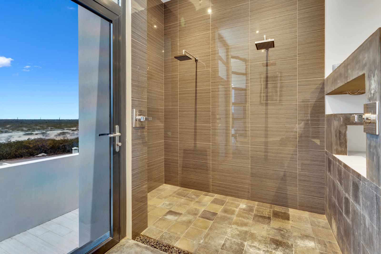Luxury Bonaire villa spa bathroom with a walk-in dual rain shower, natural stone tile, and a private balcony offering expansive views of the Caribbean landscape.